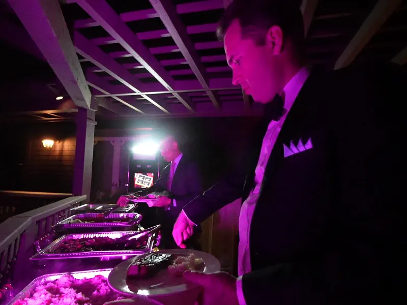 Catering attendant plating from a buffet under evening uplights at a Mill Valley hillside event