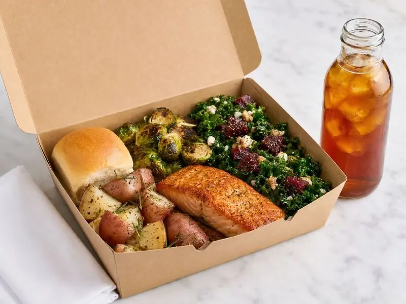 Marin Catering Company portable dinner with a salmon fillet, nutrient-rich kale salad, Brussels sprouts, potatoes, and a bakery roll.