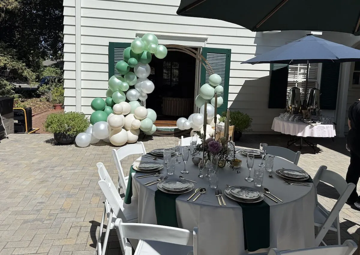 Sage and ivory balloon garland over a doorway paired with a bloom-accented tablescape — balloon and floral styling for Petaluma catering parties